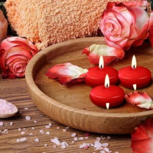 Vela flotante roja encendida en plato de madera con pétalos de rosa y sal rosa, ideal para ambiente romántico en baño.