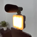 Kit de video con luz LED RGB encendida y micrófono de solapa montado sobre smartphone, ideal para grabaciones profesionales.