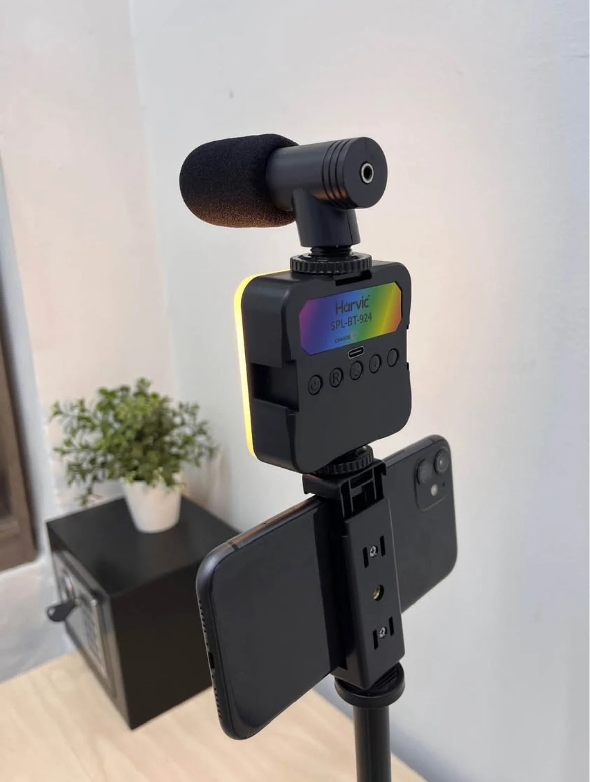 Kit de video con trípode, micrófono y luz LED RGB en color negro, mostrando dispositivo principal con pantalla RGB y micrófono montado superiormente, junto a smartphone fijado en soporte lateral.