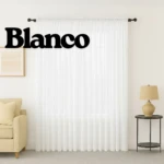 Cortina de velo muselina blanca, filtradora de luz, colgada en ventana con varilla oscura, en sala con sillón y lámpara.