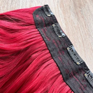 Extensiones de cabello semi humanas lisas con clips en color rojo intenso, mostrando la banda negra con cuatro clips metálicos visibles para fijación.