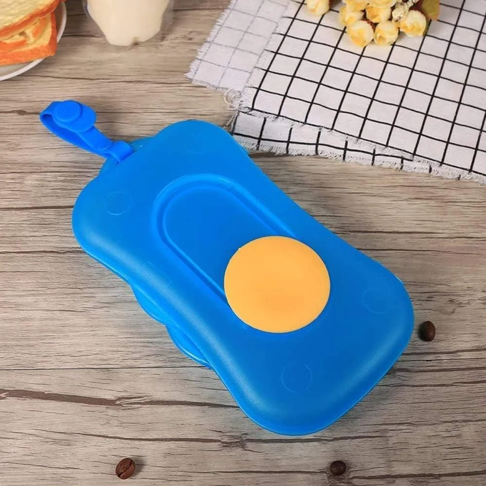 Dispensador de pañitos portátil en color azul con tapa amarilla, sobre superficie de madera con toalla de cuadros y elementos decorativos al fondo.