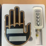 Mano LED negra con contorno amarillo, sensor de pulso y oxígeno, incluye control remoto blanco y batería en caja blanca.