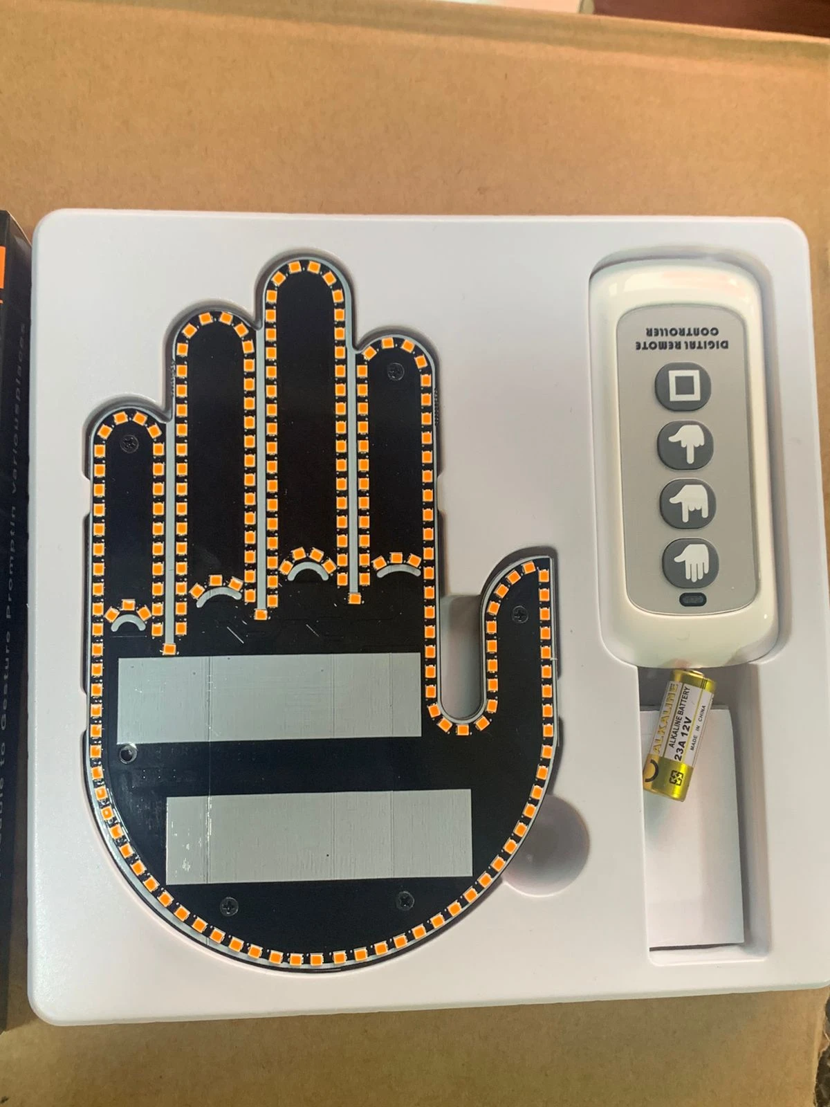 Mano LED negra con contorno amarillo, sensor de pulso y oxígeno, incluye control remoto blanco y batería en caja blanca.