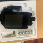 Mano LED negra con sensor de oxígeno y pulso, vista superior en caja blanca con control remoto y batería.