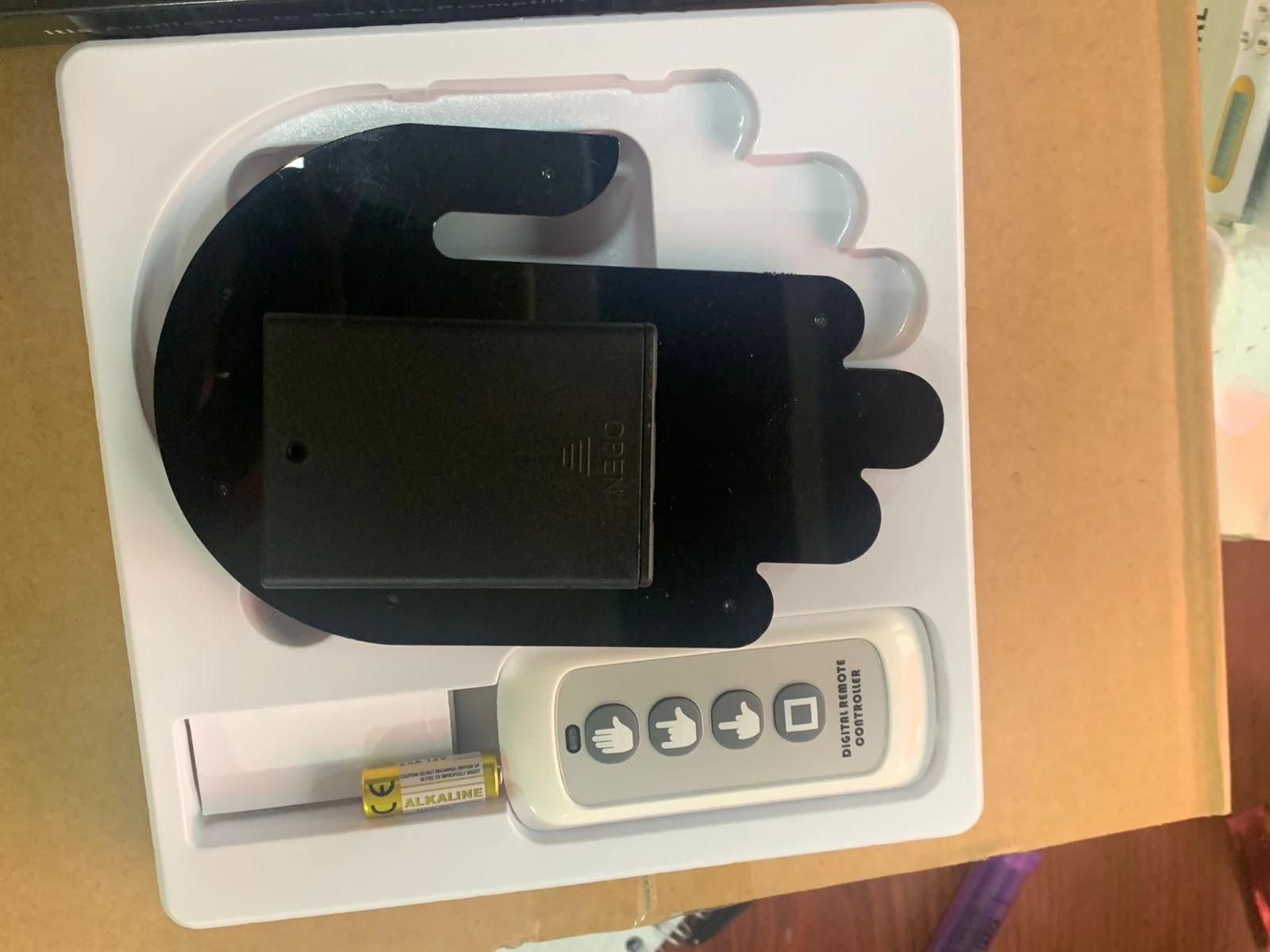Mano LED negra con sensor de oxígeno y pulso, vista superior en caja blanca con control remoto y batería.