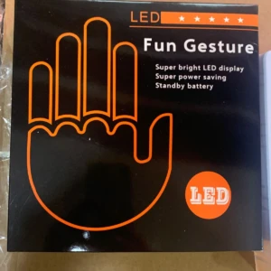 Mano LED negra con contorno naranja, mostrando cinco dedos y palma. Caja frontal con texto Fun Gesture y detalles técnicos en blanco.