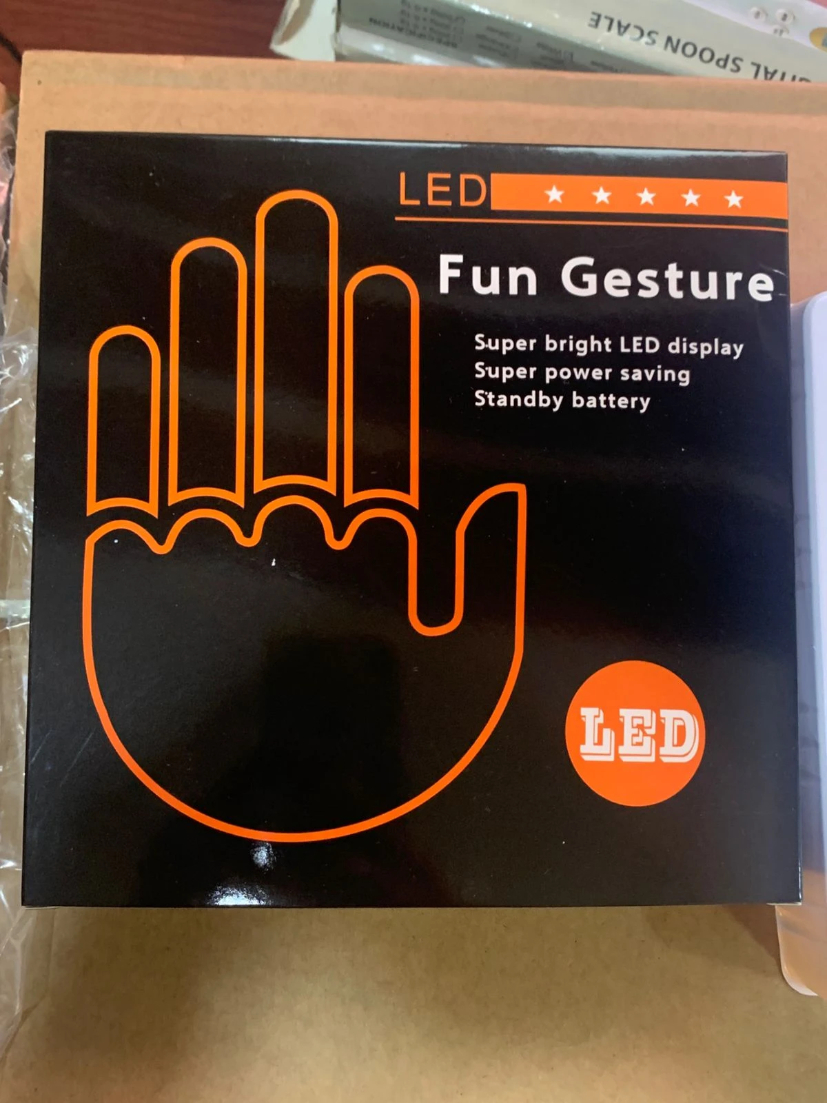 Mano LED negra con contorno naranja, mostrando cinco dedos y palma. Caja frontal con texto Fun Gesture y detalles técnicos en blanco.