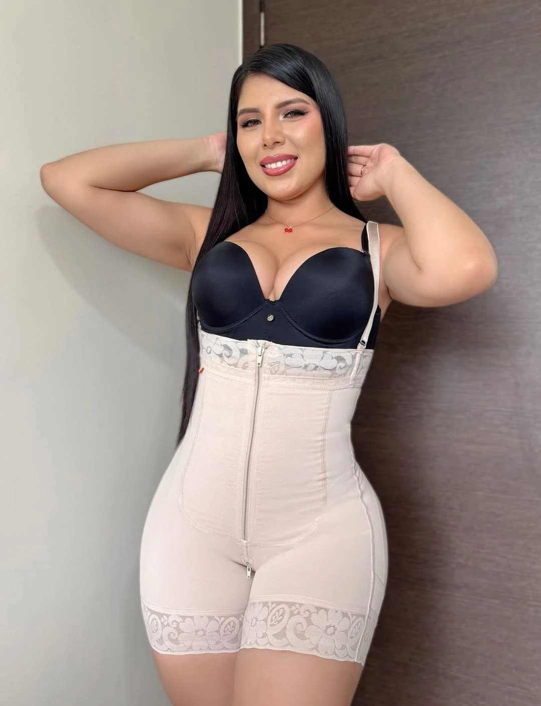 Faja modeladora cremallera frontal en color nude con top negro, vista frontal de modelo sonriendo con brazos levantados.