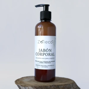 Bote de jabón corporal natural Zoieco en vidrio ámbar con dispensador negro, sobre base de madera rústica. Etiqueta blanca con texto negro y detalles florales.