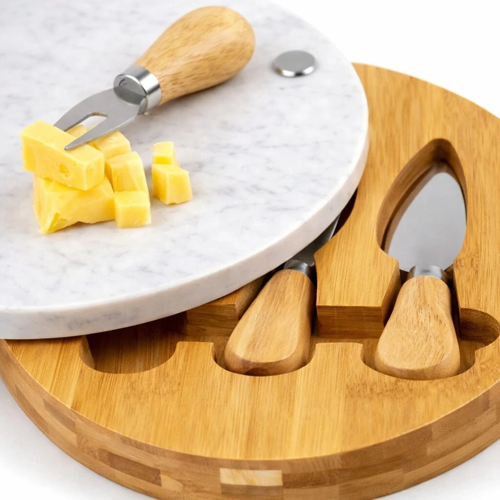 Tabla de quesos redonda con superficie de mármol blanco y base de bambú natural, incluye cuchillo de servir y dos utensilios de madera con mango, sobre fondo blanco.