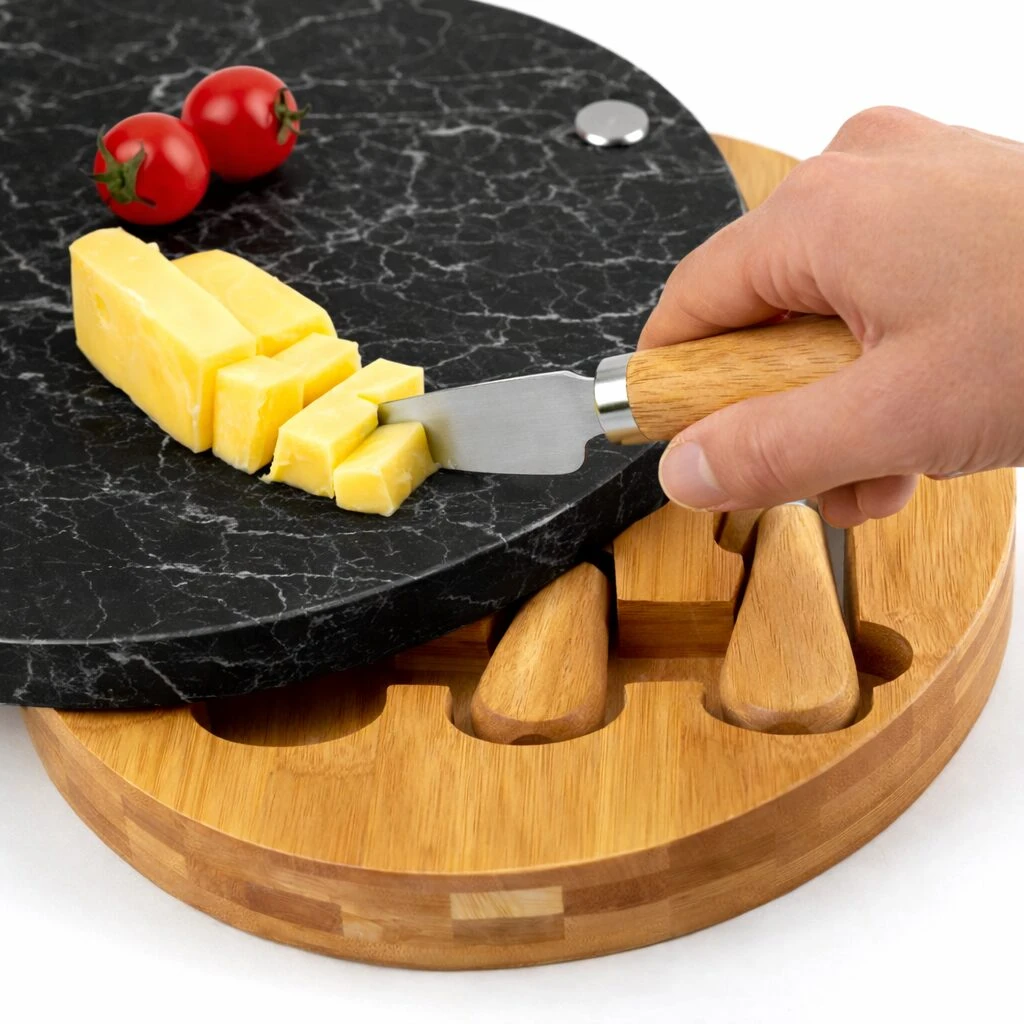 Tabla redonda de quesos con superficie de mármol negro y base de bambú, con ranuras para utensilios y queso cortado sobre ella.