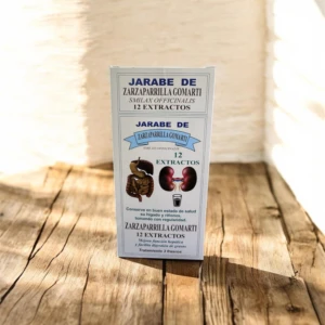 Botella de jarabe de zarzaparrilla Gomarti con 12 extractos naturales, sobre superficie de madera clara. Etiqueta blanca con detalles en azul y marrón.