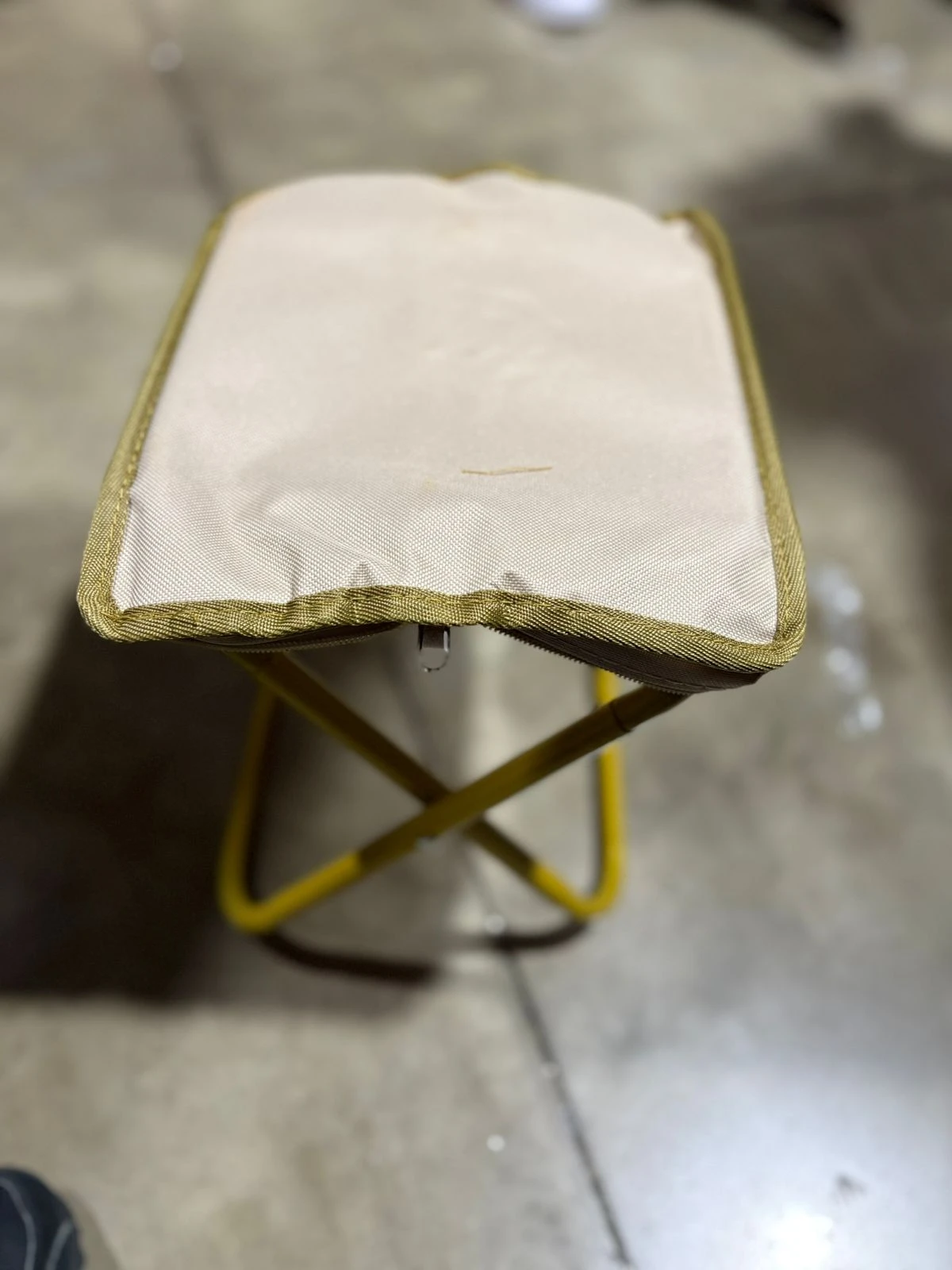 Silla plegable de acero con asiento beige y marco amarillo, vista superior mostrando costuras y textura del tejido.