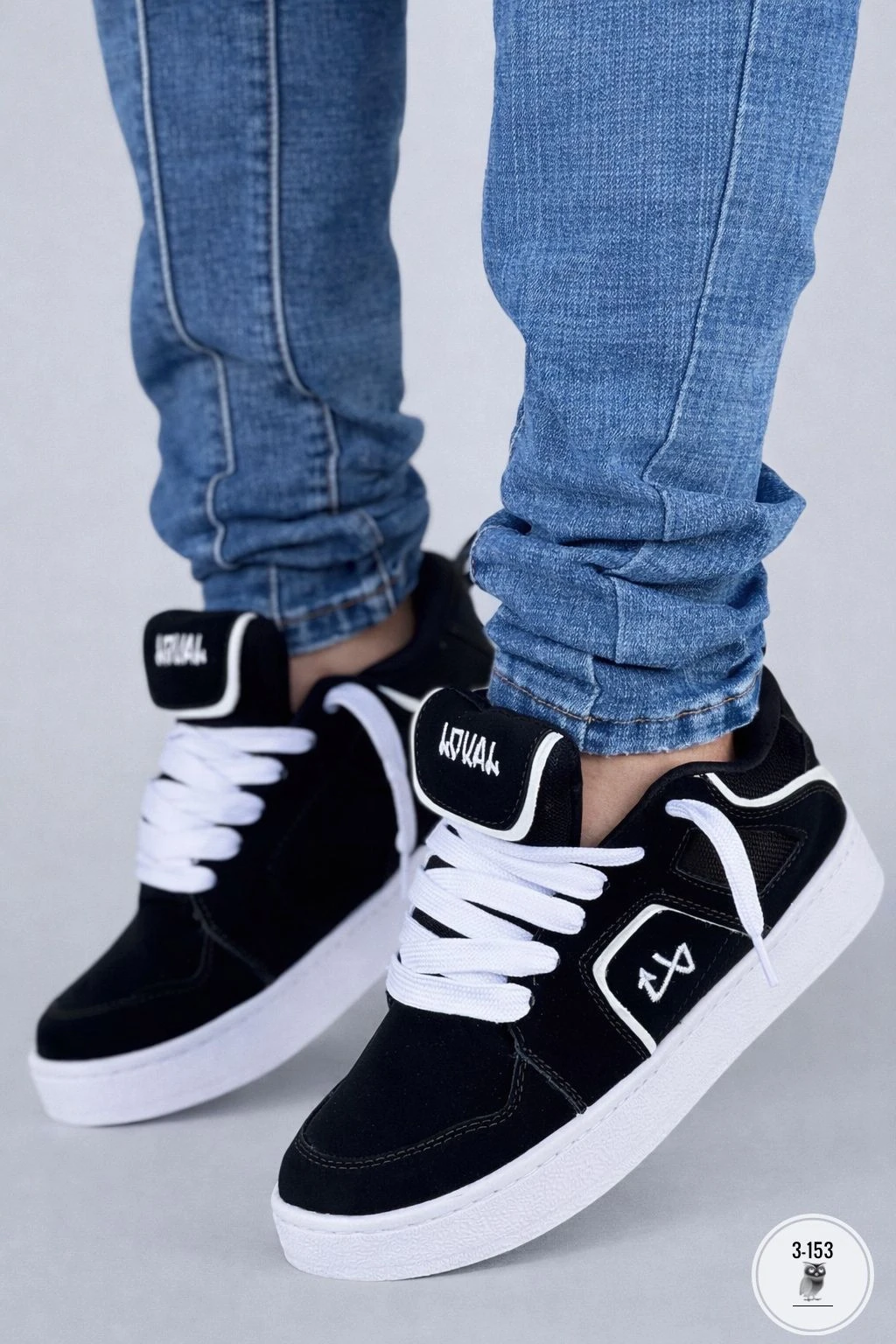 Zapatilla deportiva Lokal Colombia negra con cordones blancos y suela goma, vista frontal sobre jeans azul.