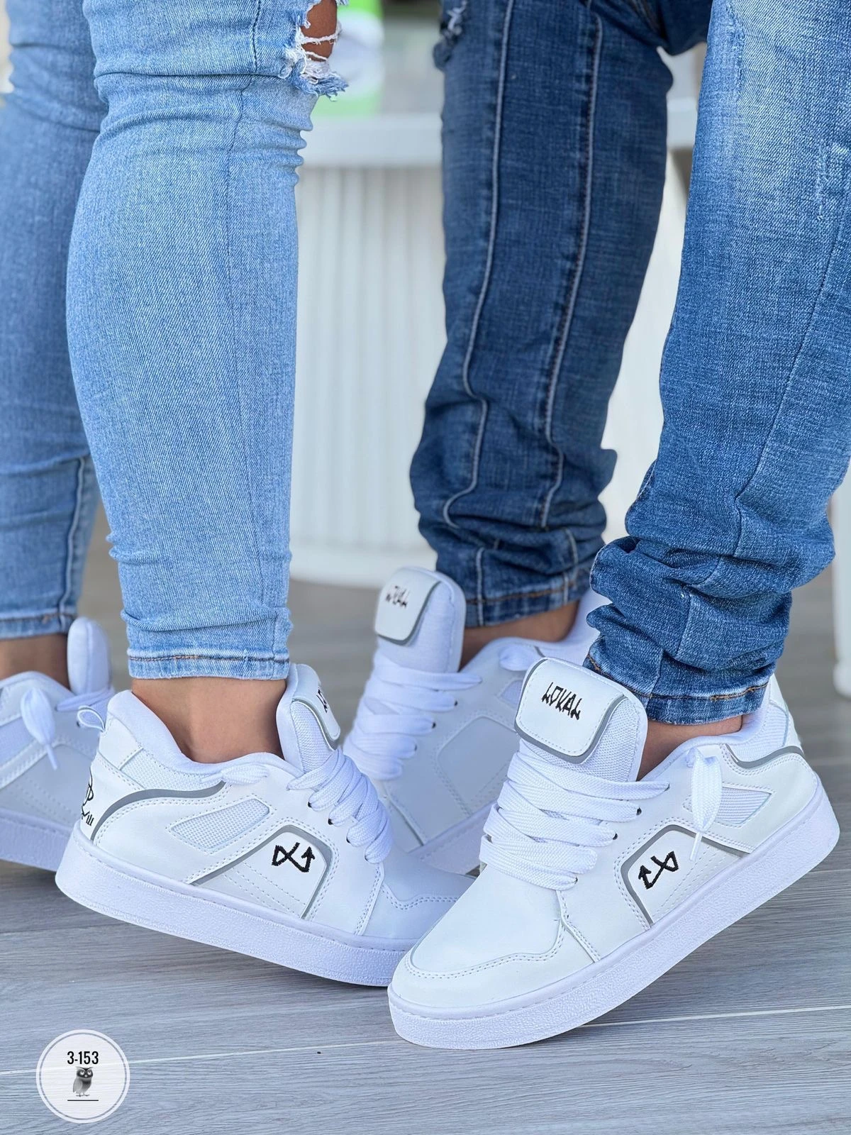 Zapatilla deportiva blanca con detalles grises, modelo Lokal, vista lateral en uso con jeans. Suela de goma visible, diseño moderno para caminar todo el día.
