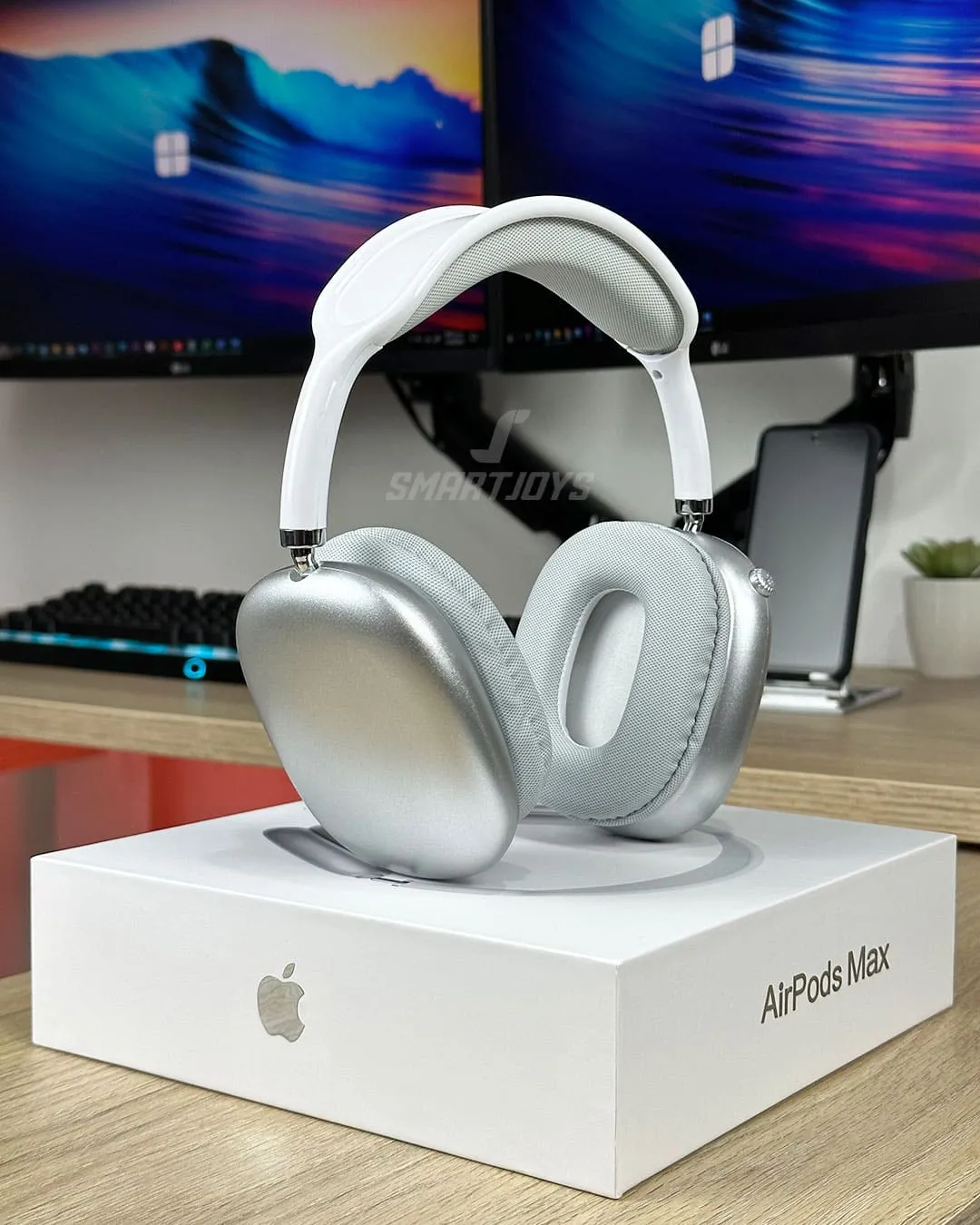 Diadema inalámbrica estilo AirPods Max en color blanco plateado, con almohadillas acolchadas y caja original Apple visible en primer plano.