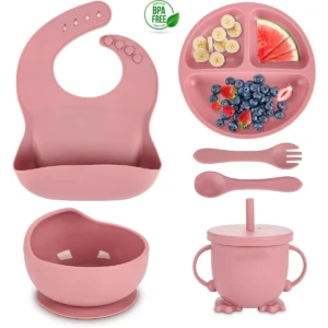 Set de vajilla para bebé en color rosa, incluye babero, plato dividido con frutas, cuchara, tenedor, taza con asa y bol con base antideslizante.