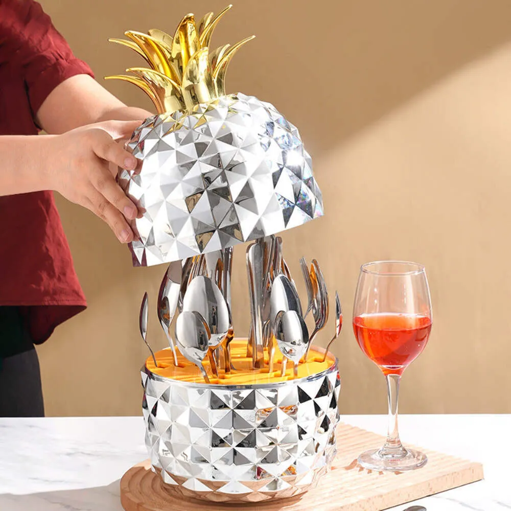 Set de cubiertos en estuche de piña con tapa removible, base y mango dorados, sobre mesa con copa de vino.