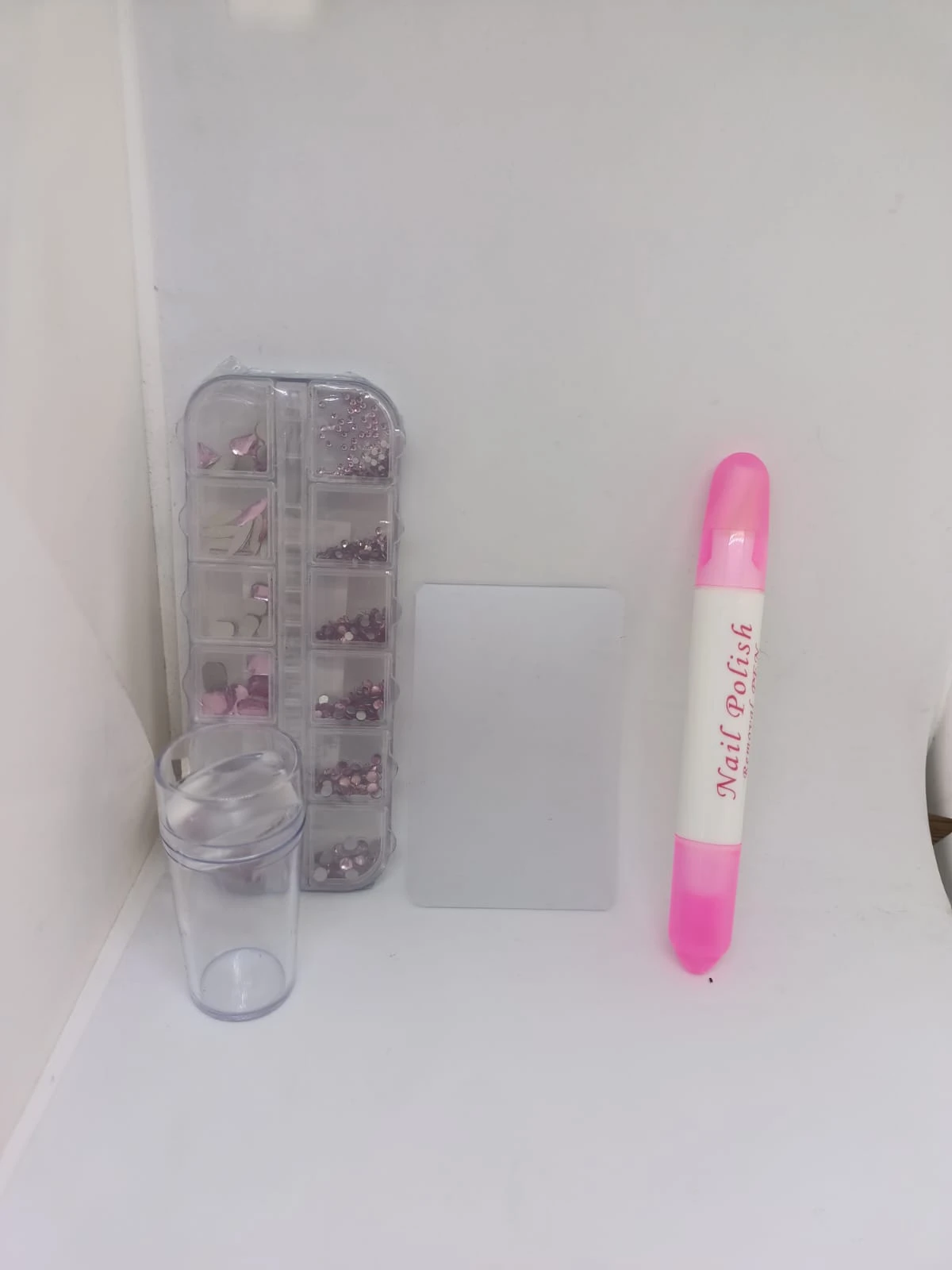 Kit de decoración para uñas con piedras y estampador. Incluye organizador de gemas, tóner, base transparente y marcador rosa con texto visible.