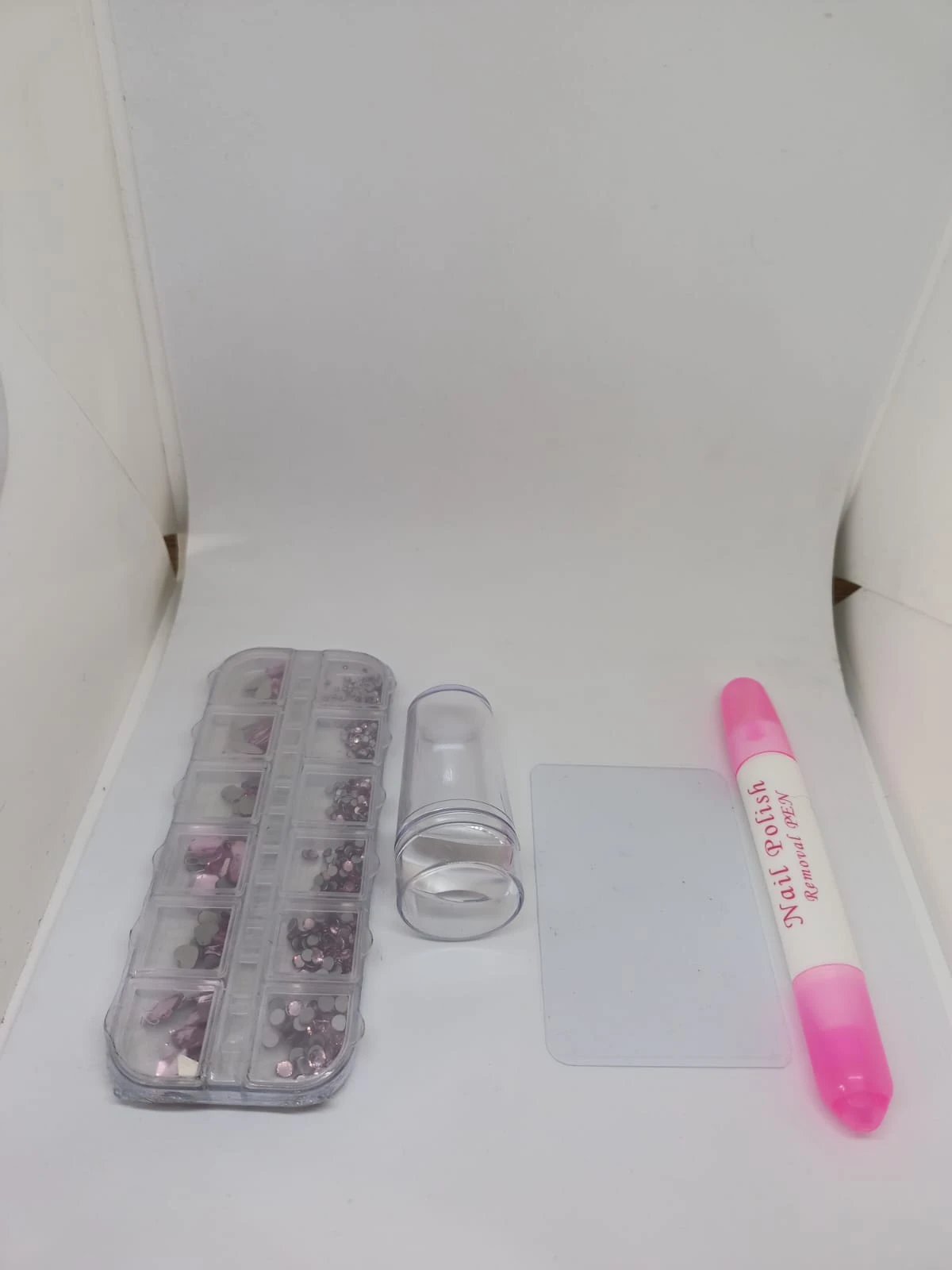 Kit de decoración para uñas con piedras y estampador. Incluye caja de compartimentos con pedrería, rodillo de silicona, plantilla y marcador rosa.