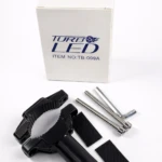 Kit de montaje para faro TK-01A: abrazadera negra con sujeción dentada, dos tiras adhesivas y tres tornillos hexagonales, junto a caja blanca con logo Turb LED.