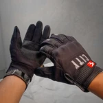 Guante negro de conducción con tacto táctil, mostrando palma y dorso con detalles en malla y logo rojo visible en muñeca.