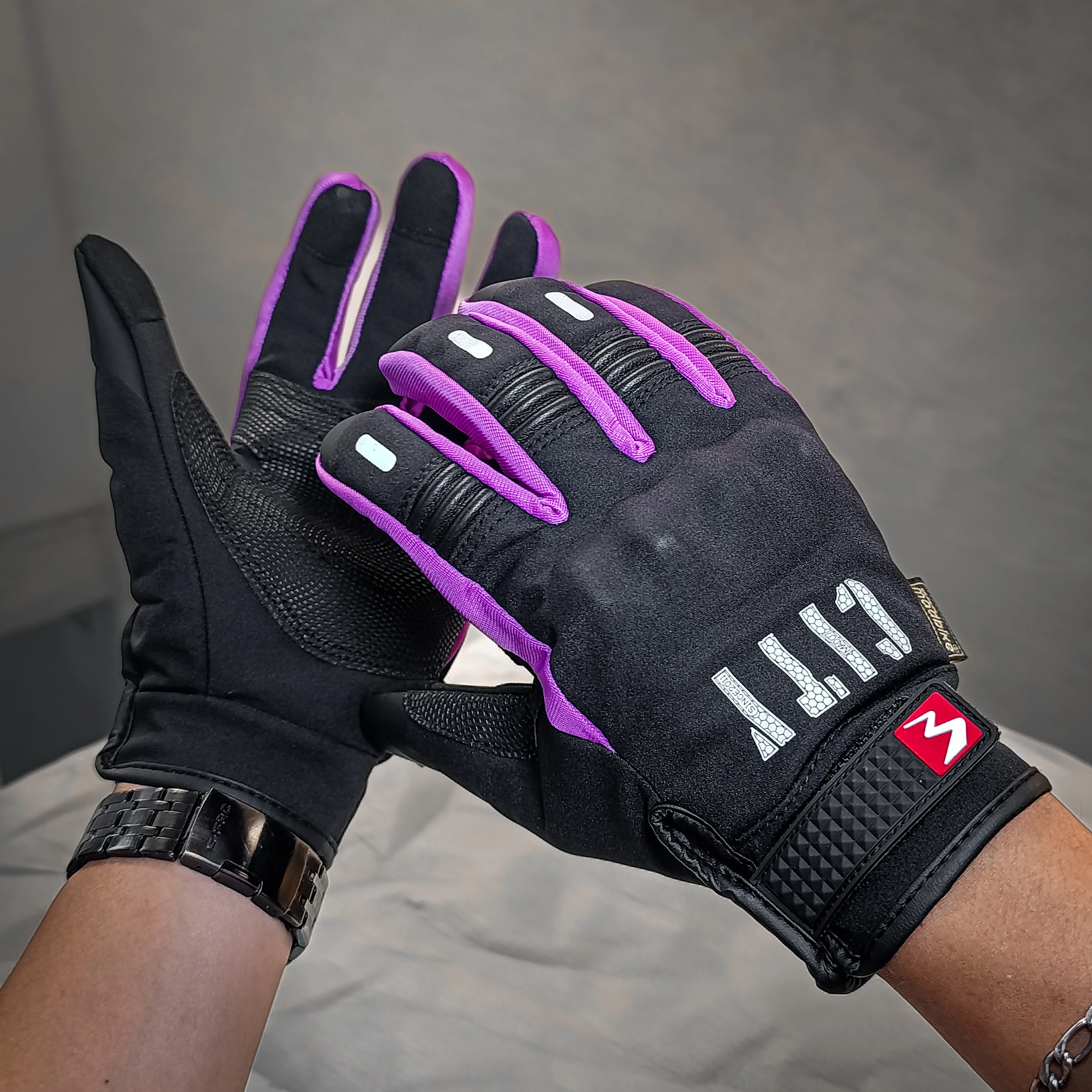 Guante City negro con detalles en morado, diseño táctil para uso en el celular mientras se conduce, con logo visible en la muñeca.