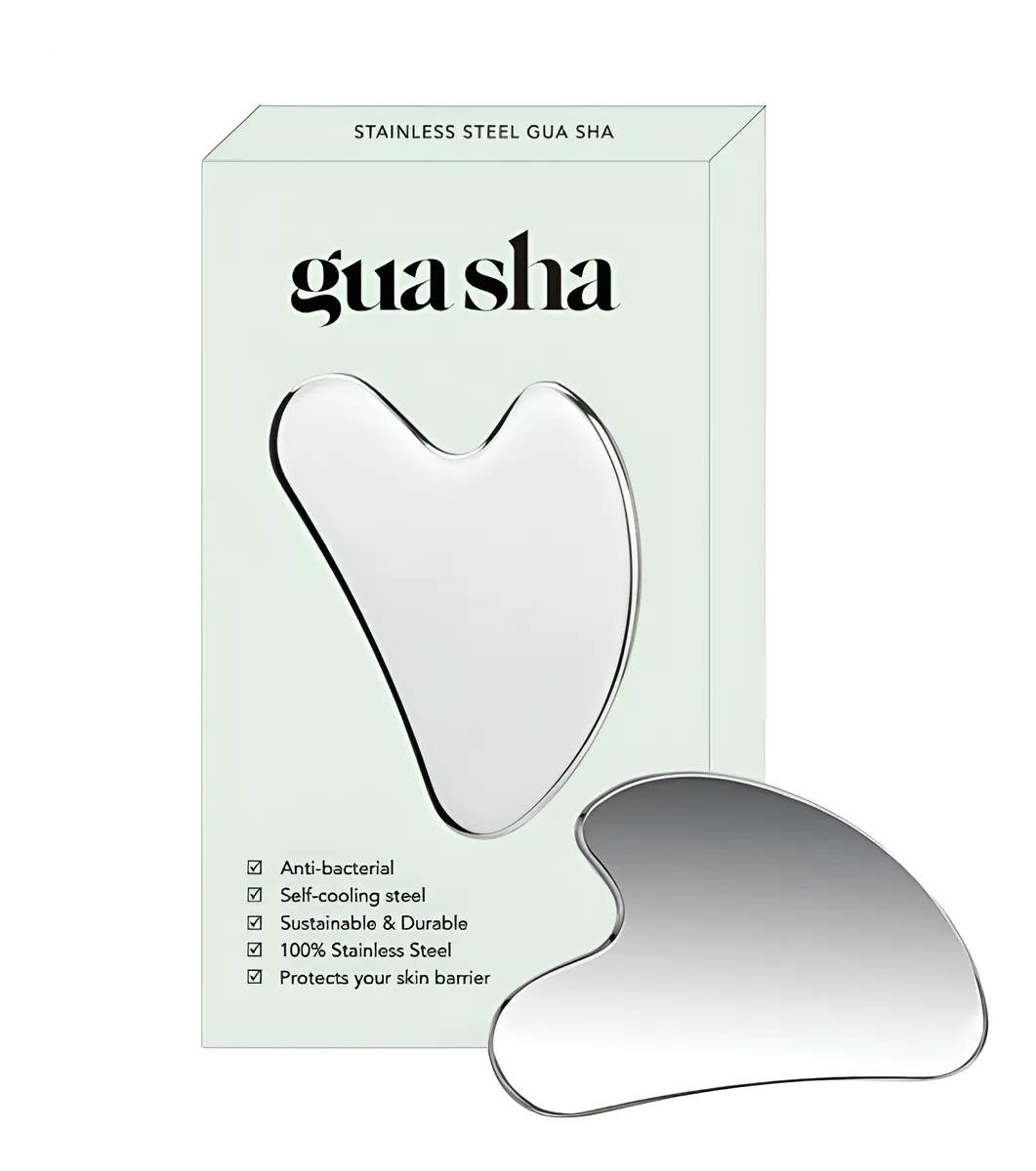 Gua sha de acero inoxidable en color plateado, con forma ergonómica y acabado pulido, acompañado de su caja de presentación en tono verde claro.