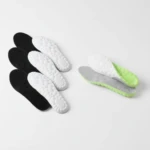 Plantillas deportivas acolchadas en blanco y negro, con base antideslizante verde y gris, mostrando textura de suela y diseño ergonómico para caminar.