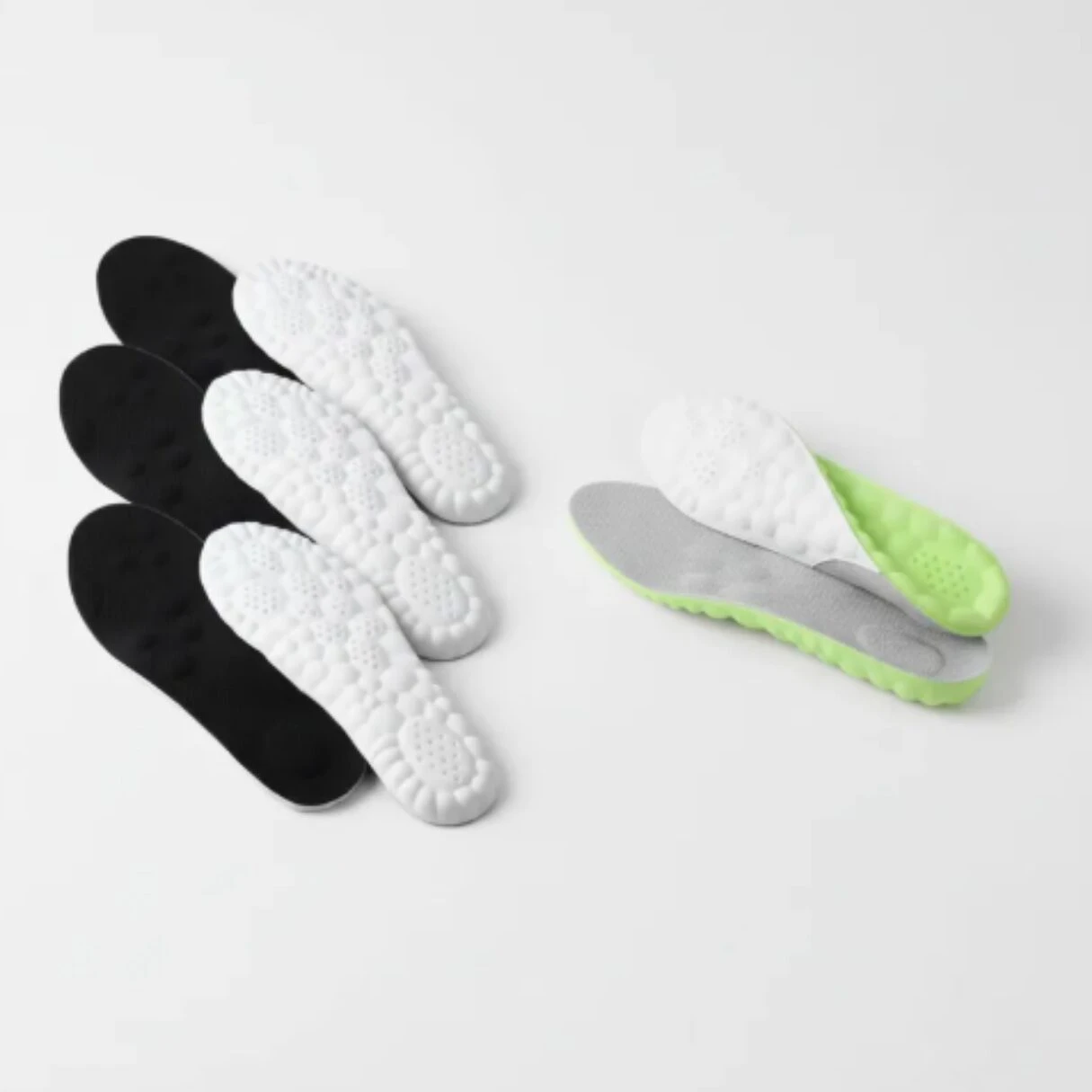 Plantillas deportivas acolchadas en blanco y negro, con base antideslizante verde y gris, mostrando textura de suela y diseño ergonómico para caminar.