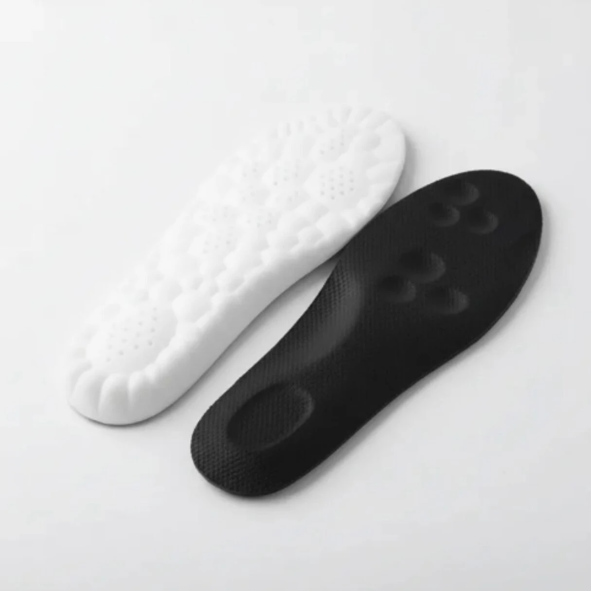 Plantillas deportivas acolchadas en blanco y negro, con base antideslizante y diseño ergonómico para mejorar estabilidad y reducir fatiga al caminar.