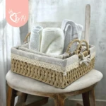 Canasta tejida de ratan cuadrada con forro beige, mostrando toallas enrolladas y plegadas dentro, sobre silla de madera clara.