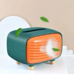 Dispensador de servilletas estilo radio retro en verde y naranja, con ventilador frontal y patas de madera, sobre superficie blanca.