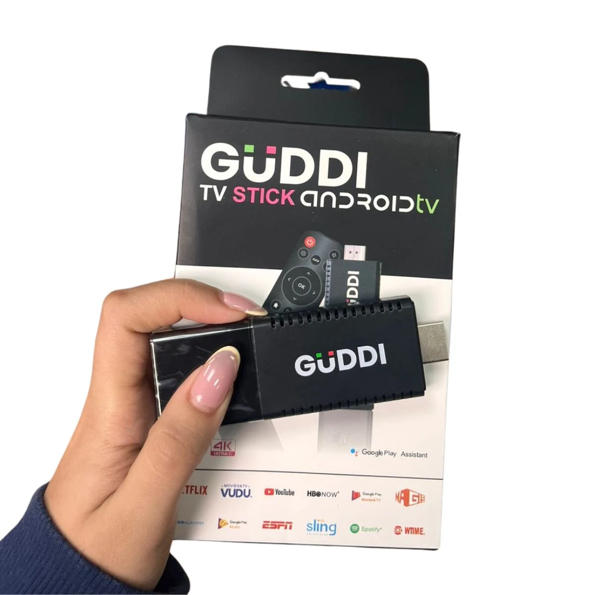 TV Stick Guddi negro con control remoto incluido, mostrando el dispositivo en su empaque original con logotipos de plataformas de streaming visibles en la caja.