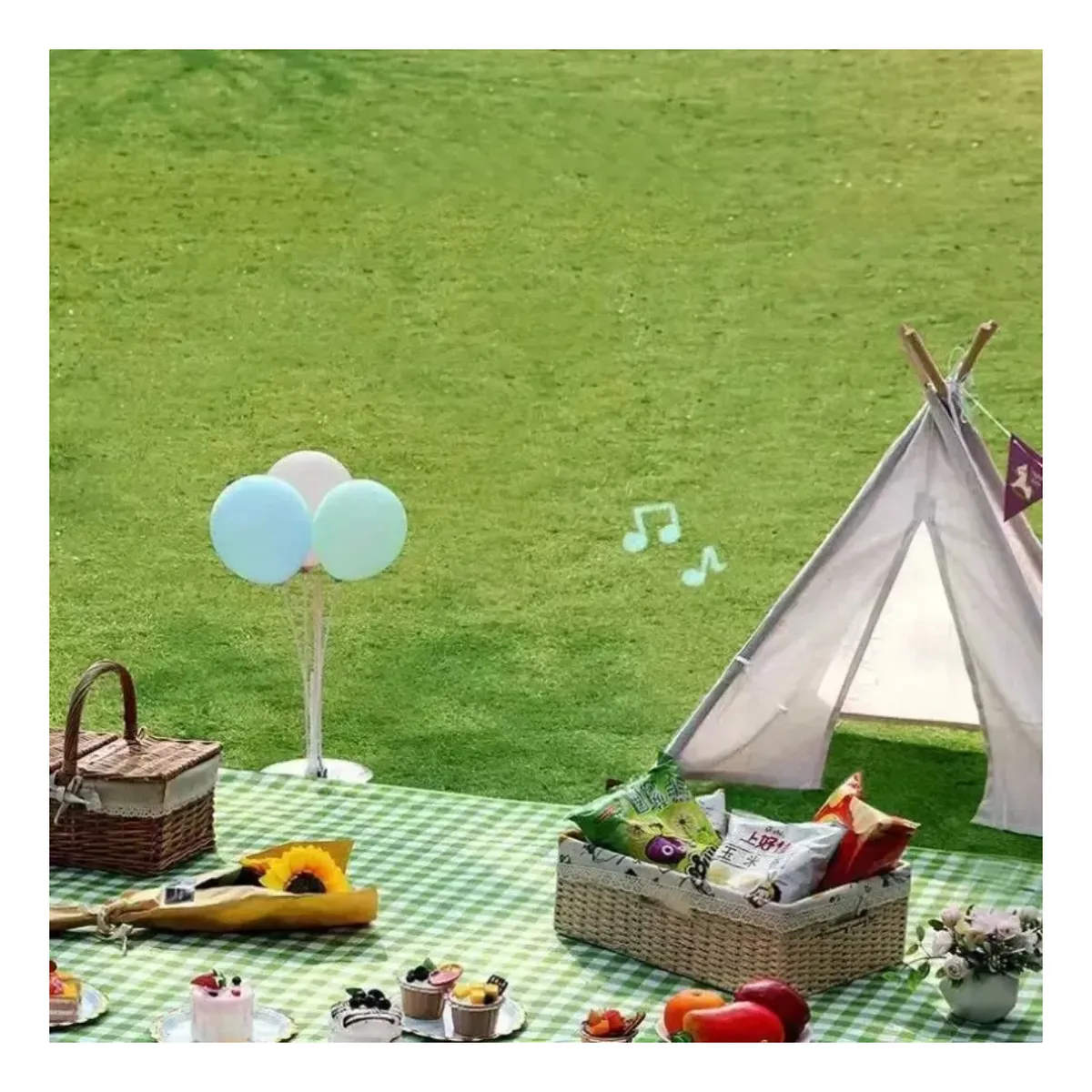 Alfombra picnic a cuadros verdes y blancos con cesta de mimbre, globos pastel, flores y accesorios de picnic sobre césped verde.