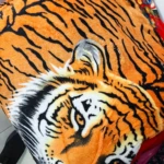 Cobija térmica de felpa con estampado realista de tigre en tonos naranjas y negros, vista frontal mostrando cabeza y patas.