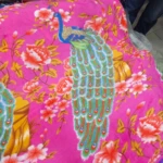 Cobija térmica rosa con diseño de pavo real y flores, vista frontal mostrando textura suave y estampado completo.