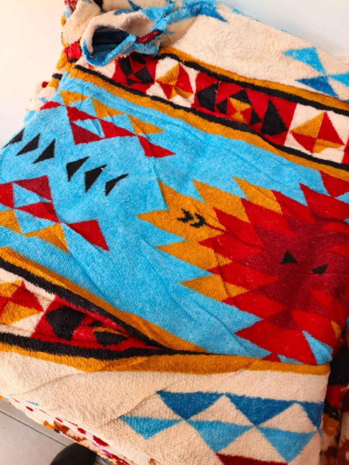 Cobija térmica para cama doble con diseño geométrico en tonos azul, rojo y amarillo, textura suave y bordes decorativos.