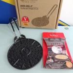 Parrilla para arepas de hierro fundido, color negro, con mango y caja original Victoria, junto a su empaque rojo.