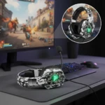 Diadema gamer Onikuma K8 en camuflaje blanco con luces LED verdes, micrófono ajustable y auriculares sobre teclado RGB y monitor de videojuegos.