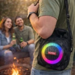 Bolso parlante negro con luces LED multicolor y logo rojo, usado por hombre en ambiente nocturno junto a fogata.