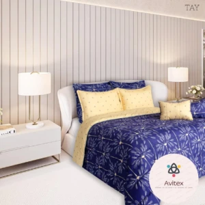 Edredón acolchado doble faz en azul con estampado floral y cojines amarillos sobre cama blanca, en habitación moderna con lámparas y pared vertical.
