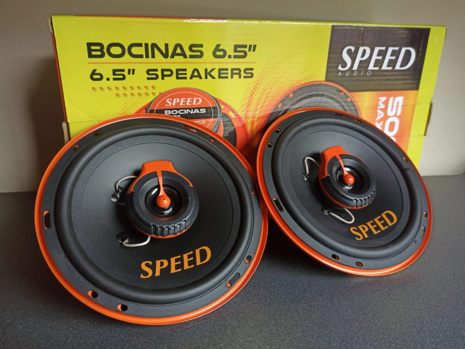 Dos parlantes automotrices Speed de 6.5 pulgadas, color negro con detalles naranjas, montados sobre una caja amarilla que indica 500W.