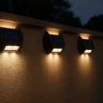 Tres lámparas solares exteriores de color negro instaladas en pared texturizada, emitiendo luz cálida en ambiente nocturno.