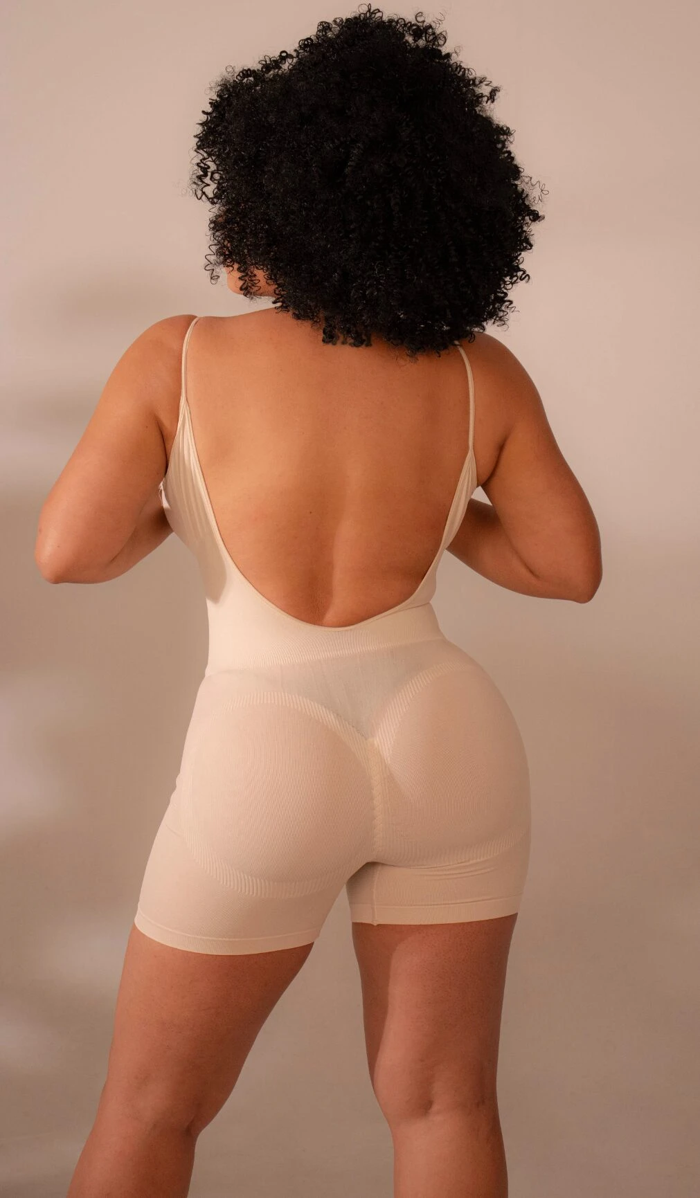 Faja moldeadora color crema con espalda descubierta, vista posterior en modelo con cabello rizado.