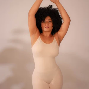 Faja moldeadora color crema, espalda descubierta, define cintura y mejora postura. Modelo con cabello afro, brazos levantados cruzados.