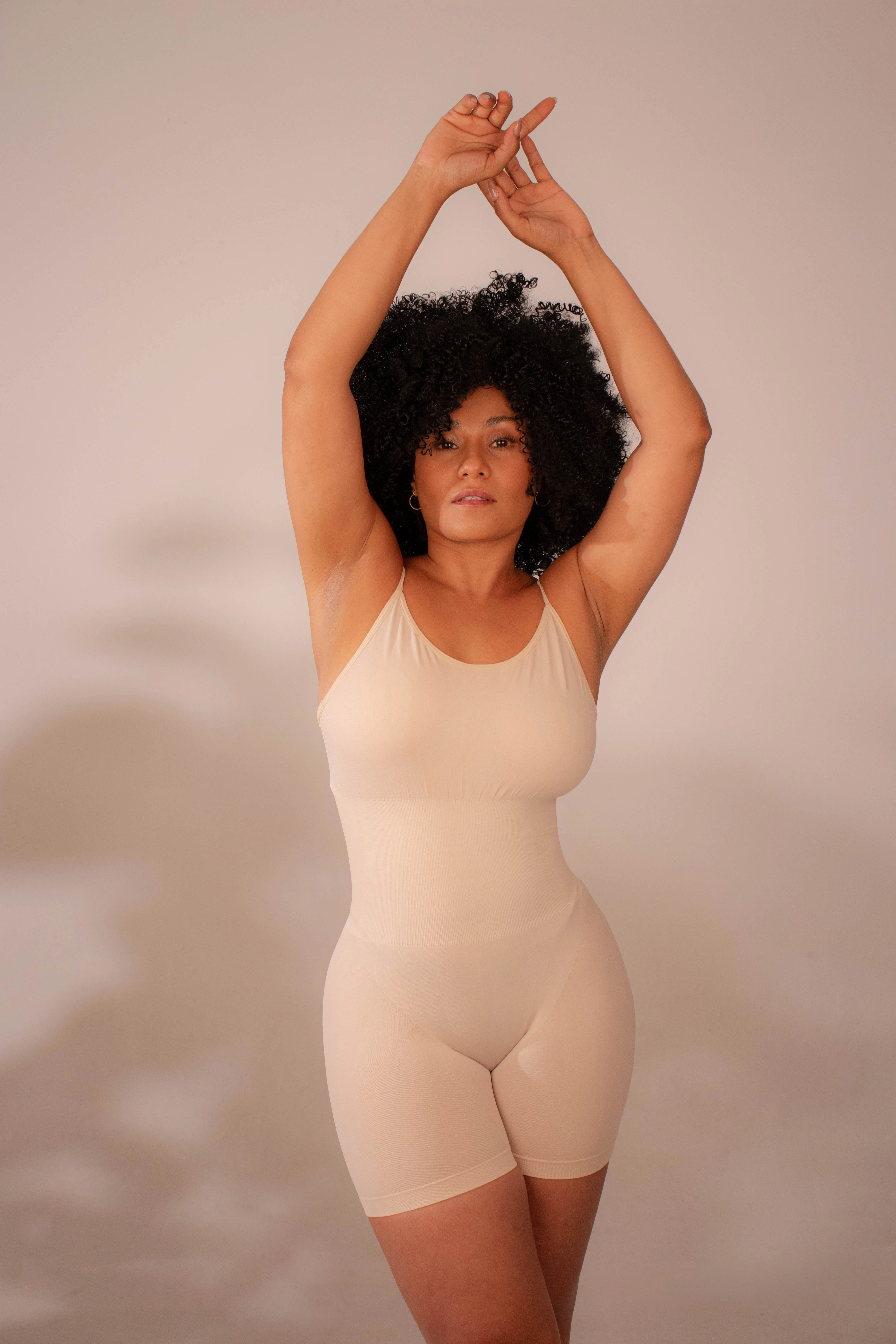 Faja moldeadora color crema, espalda descubierta, define cintura y mejora postura. Modelo con cabello afro, brazos levantados cruzados.