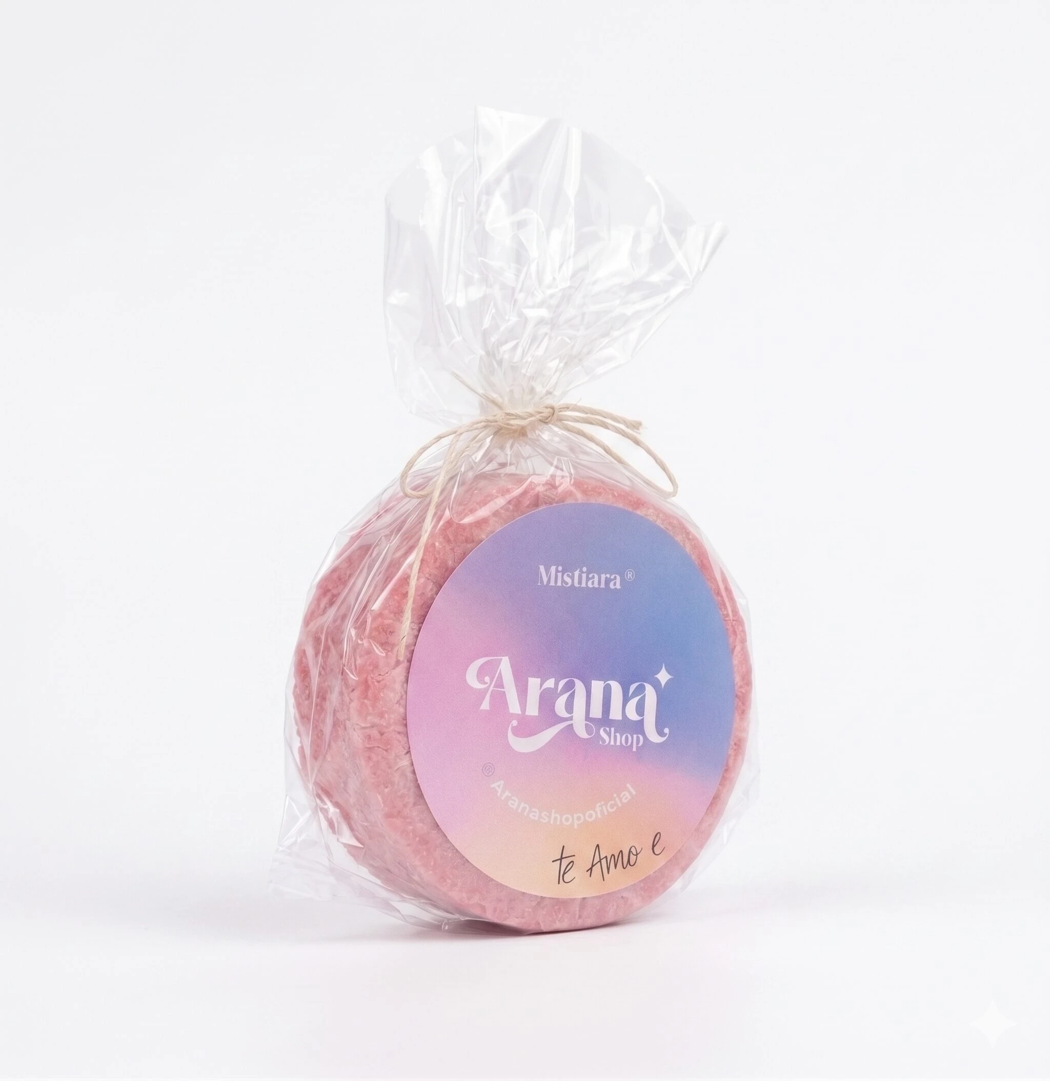 Jabón artesanal redondo de color rosa envuelto en plástico transparente con etiqueta multicolor que dice Arana Shop.