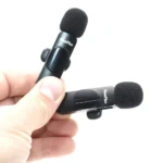 Dos micrófonos de solapa N8 Plus tipo C en color negro, con funda antichoque y clip de sujeción, sostenidos en mano sobre fondo blanco.